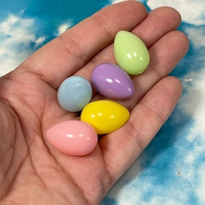 May include: Five pastel-colored plastic Easter eggs in a hand. The eggs are light blue, light green, light pink, light yellow, and light purple.
