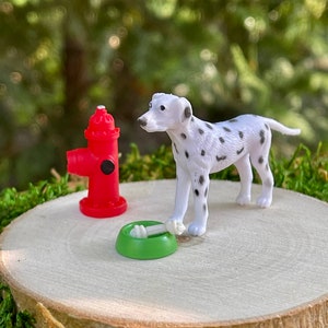 May include: A miniature dalmatian dog figurine standing next to a red fire hydrant and a green dog bowl with a bone inside. The figurines are on a wooden base.