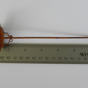 May include: A decorative metal garden stake with a brown stem and a green and brown top. The stake is approximately 10 inches long.