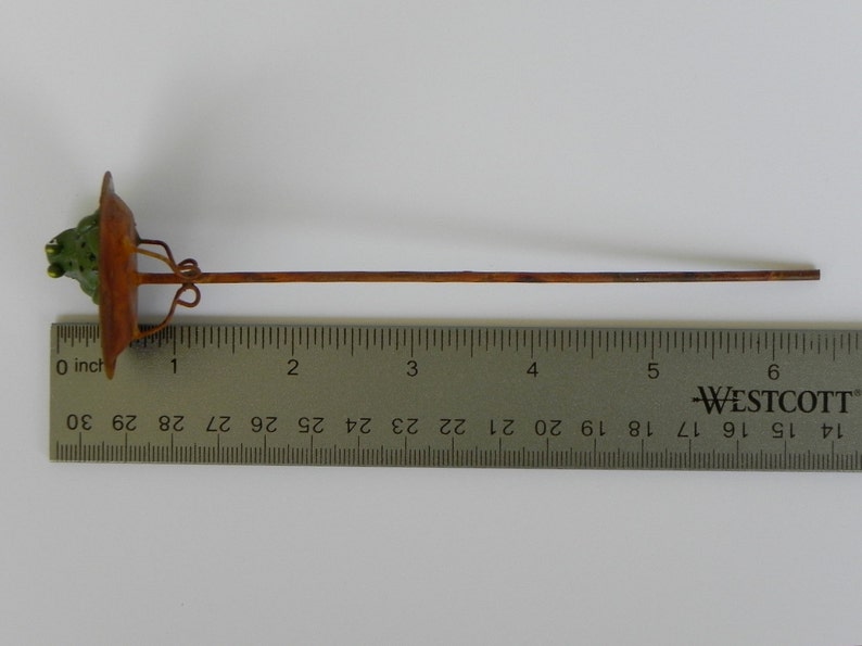 May include: A decorative metal garden stake with a brown stem and a green and brown top. The stake is approximately 10 inches long.