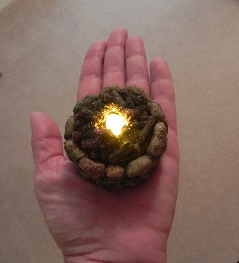 May include: A small, realistic-looking campfire with glowing embers, made of brown and gray materials, and a light inside.