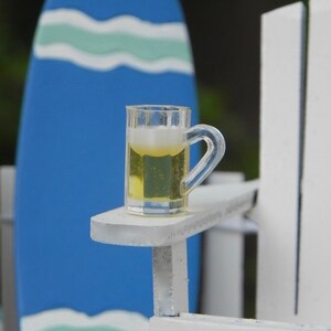 May include: A white wooden chair with a glass of beer on the armrest. The chair is in front of a blue and white surfboard.