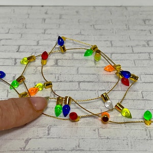 May include: A string of miniature Christmas lights with colorful bulbs in red, green, blue, yellow, and orange. The lights are strung on a gold wire, perfect for holiday decorations.