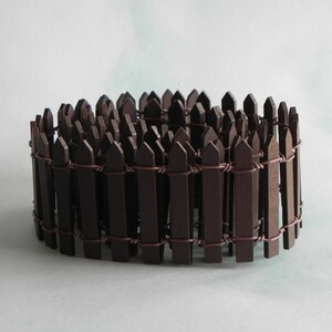 May include: A brown wooden picket fence with wire connecting the pickets. The fence is curved into a circle.