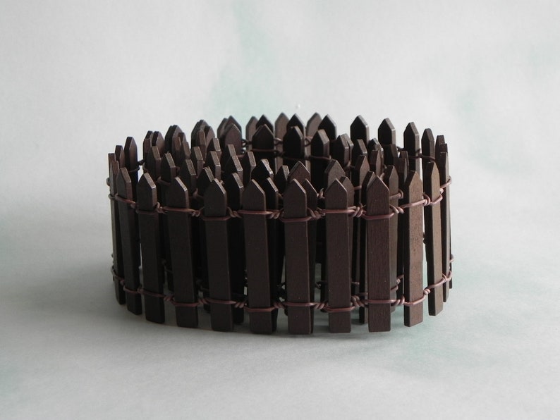 May include: A brown wooden picket fence with wire connecting the pickets. The fence is curved into a circle.