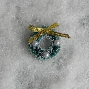 May include: A small green Christmas wreath with white beads and a gold ribbon bow.