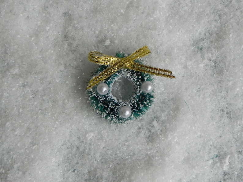 May include: A small green Christmas wreath with white beads and a gold ribbon bow.