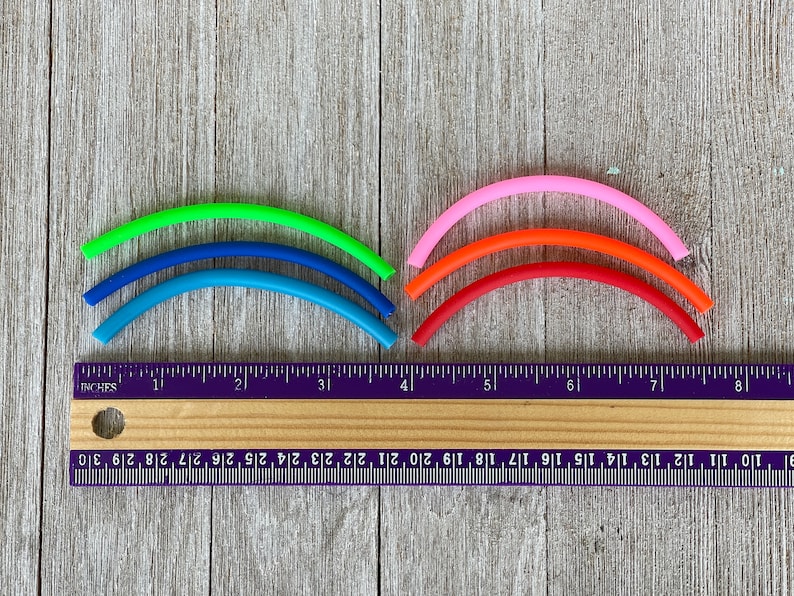 May include: Five colourful rubber bands in a rainbow pattern, measured against a ruler. The bands are green, blue, light blue, orange, and pink.