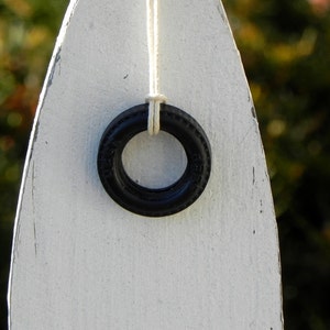 Peut inclure: Un anneau en caoutchouc noir suspendu &agrave; une ficelle blanche sur une surface en bois blanc. L'anneau a un diam&egrave;tre d'environ 5 cm.