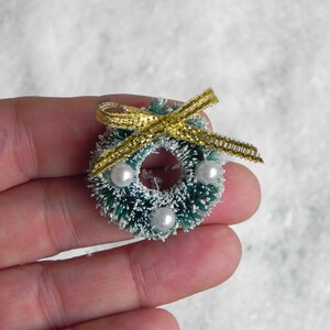 May include: A small green and white Christmas wreath with a gold ribbon and white pearl accents.