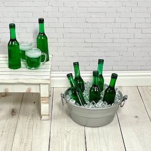 May include: A silver metal bucket filled with ice and six green glass bottles of beer. The bucket is sitting on a white wooden surface.