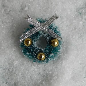 May include: A small green Christmas wreath with gold ornaments and a silver bow.