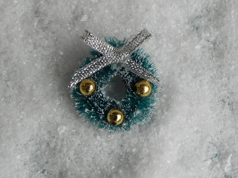May include: A small green Christmas wreath with gold ornaments and a silver bow.