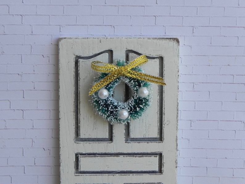 May include: A green Christmas wreath with white beads and a yellow bow hanging on a white door.