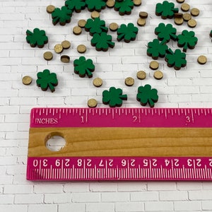 May include: A close-up of a ruler measuring green four-leaf clover shapes and gold circles. The ruler is marked in inches.