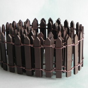 May include: A brown wooden picket fence with wire connecting the pickets. The fence is curled into a circle.