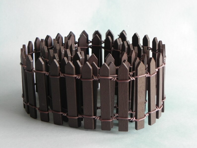 May include: A brown wooden picket fence with wire connecting the pickets. The fence is curled into a circle.