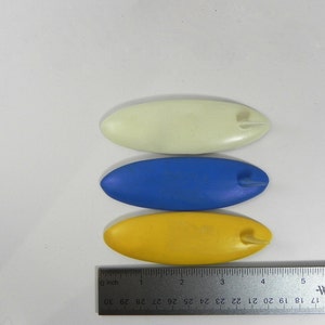 May include: Three plastic craft tools, shaped like surfboards, in yellow, blue, and white.