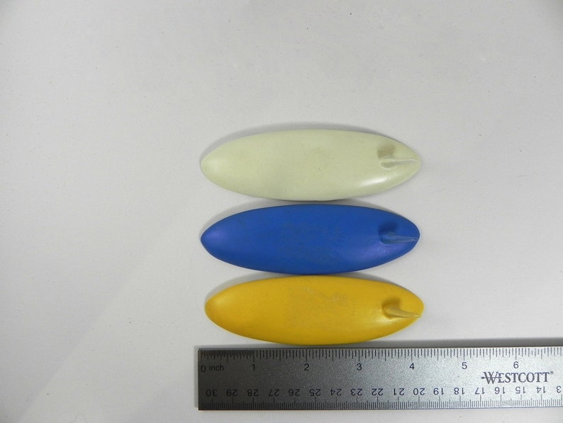 May include: Three plastic craft tools, shaped like surfboards, in yellow, blue, and white.