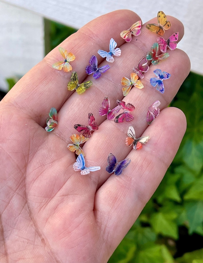 May include: A collection of colorful butterfly embellishments, perfect for crafting and adding a touch of whimsy to projects. The butterflies are made of clear plastic with printed designs and come in a variety of colors, including pink, blue, yellow, green, and purple.
