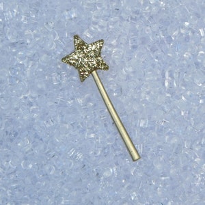 May include: A gold glitter star-shaped wand with a silver handle on a white background.