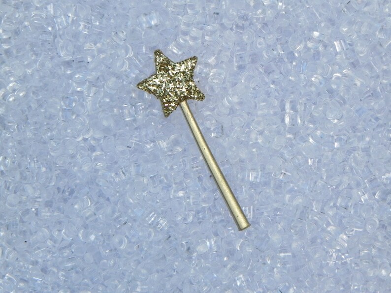 May include: A gold glitter star-shaped wand with a silver handle on a white background.