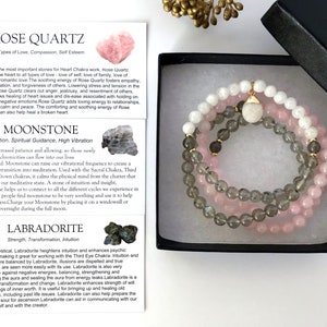 Puede incluir: Tres pulseras apiladas hechas con cuentas de cuarzo rosa, piedra lunar y labradorita. Las pulseras están en una caja negra con papel de seda blanco. La imagen incluye texto que describe las propiedades de cada piedra.