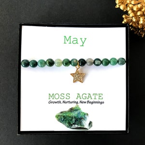 May include: A green moss agate bracelet with a gold star charm. The bracelet is in a black box with a white card that says "May" and "Moss Agate, Growth, Nurturing, New Beginnings".