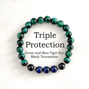 May include: A beaded bracelet with green and blue tiger eye stones, black tourmaline, and navy blue beads. The bracelet is labeled "Triple Protection". The beads are strung together with gold-colored accents.