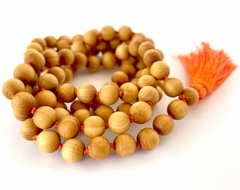 May include: A wooden mala bead necklace with a tassel. The beads are a light brown color and the tassel is a bright orange color.