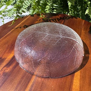 May include: A clear glass bowl with a leaf pattern. The bowl is round and has a textured surface. The bowl is sitting on a wooden surface.