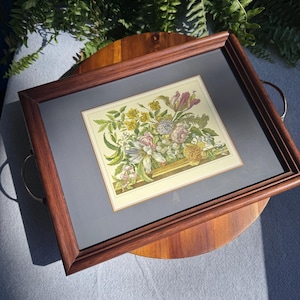 May include: A framed floral print featuring a colorful bouquet of flowers in shades of yellow, pink, purple, and white. The print is set against a gray mat and enclosed in a dark brown wooden frame with brass handles.