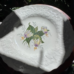 May include: A white ceramic mug with a black handle and the text "But First, Coffee" in a bold, black font. The mug is set against a blurred background, suggesting a cozy setting. The mug appears to be approximately 4 inches tall.