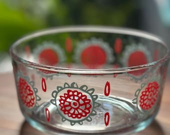 May include: Clear glass bowl with red and gray floral designs. The bowl has an oval shape and sits on a wooden surface. The floral pattern includes red flower-like shapes with gray outlines and teardrop accents.