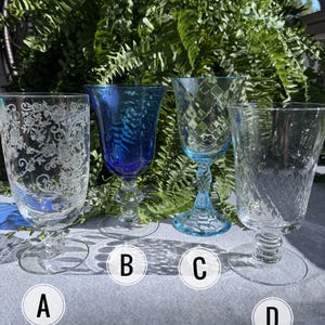May include: Four vintage wine glasses with different designs. Glass A has a floral pattern, glass B is blue, glass C is light blue with a diamond pattern, and glass D is clear with a diamond pattern. All have stems and round bases.