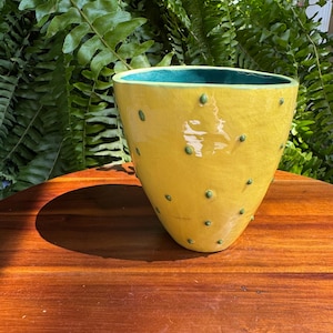 May include: A yellow ceramic planter with a glossy crackle glaze finish and small, raised green dots scattered across the exterior. The interior of the vessel is a deep teal colour, and the shape is tapered with a wide, open circular rim.