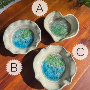May include: Three ceramic bowls with wavy edges and a light beige exterior. Each bowl features a center filled with textured, translucent glass in shades of blue and green. The bowls are labeled A, B, and C, with bowl A having a heart-shaped rim.