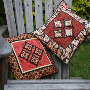 May include: Two red and gold patterned throw pillows on a wooden chair. The pillows have a geometric design with black accents.
