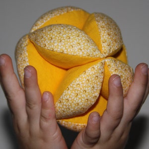 May include: A yellow fabric ball with a white floral pattern. The ball is made of multiple fabric pieces sewn together.