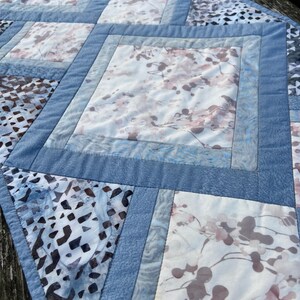 Op de afbeelding: Een blauwe en witte gestikte tafelrunner met een geometrisch patroon. De runner is gemaakt van verschillende stoffen met een verscheidenheid aan patronen, waaronder bloemen- en geometrische ontwerpen.