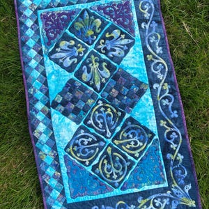 May include: A blue and purple quilt with a geometric pattern and floral designs. The quilt is made with a variety of fabrics and has a quilted texture.