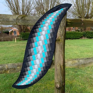 Puede incluir: Un camino de mesa acolchado de color negro, gris y turquesa con forma curva. El camino de mesa está colgado en una valla de madera.