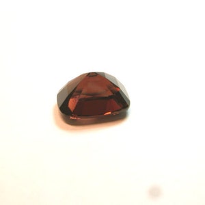 May include: A dark red gemstone with a faceted cut. The gemstone is set in a square shape.