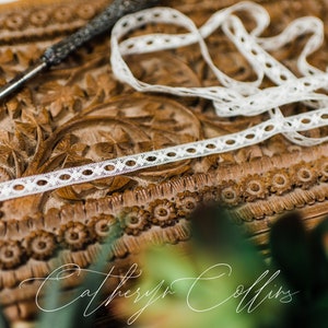 May include: White lace trim with a delicate pattern, resting on a carved wooden surface. The lace is thin and has a subtle sheen.