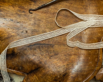 Puede incluir: Primer plano de una superficie de madera con una cinta de encaje blanca. La cinta es delicada y tiene un patrón sutil.