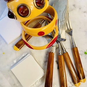 May include: A set of four vintage bakelite handled cake forks and a butter knife. The handles are a marbled brown and yellow color with a red and yellow accent. The forks and knife are silver.