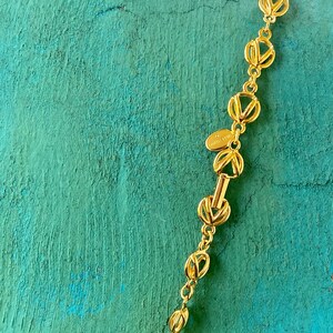 May include: A gold chain necklace with a repeating interlocking V pattern. The chain has a clasp with the text "TOMMY HILFIGER" on it.
