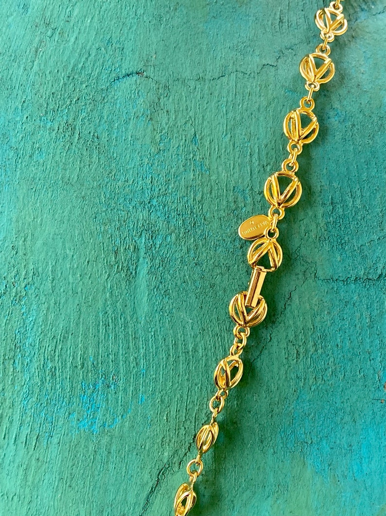 May include: A gold chain necklace with a repeating interlocking V pattern. The chain has a clasp with the text "TOMMY HILFIGER" on it.