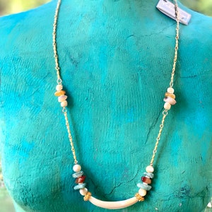 Puede incluir: Un collar de cadena dorada con un colgante curvo blanco y cuentas de piedras preciosas multicolores. Las cuentas son en tonos de marr&oacute;n, verde, rojo y blanco.