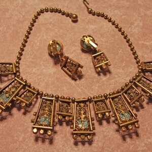 Puede incluir: Un collar de oro con una cadena delicada y m&uacute;ltiples colgantes rectangulares. Cada colgante presenta un dise&ntilde;o de filigrana y una piedra azul turquesa. Tambi&eacute;n se incluyen pendientes a juego con el mismo dise&ntilde;o.